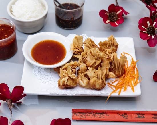 Eight crab rangoon rolls with sweet chili sauce and shredded carrot on a white plate